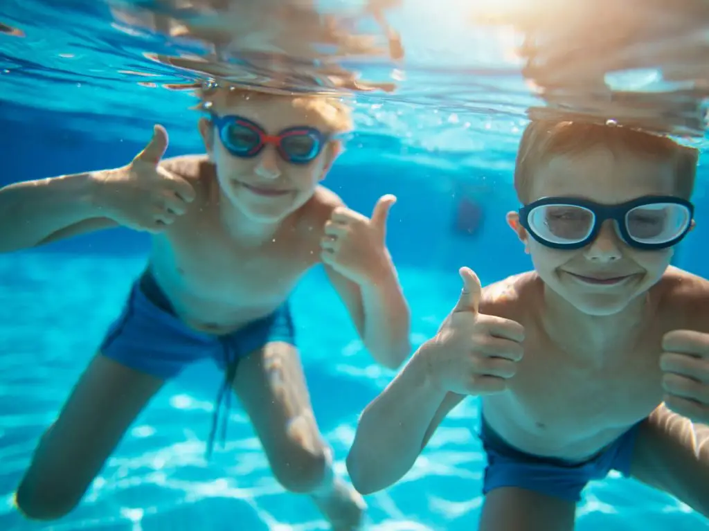 Two children giving the thumbs up under water in a freshly cleaned and maintananced pool